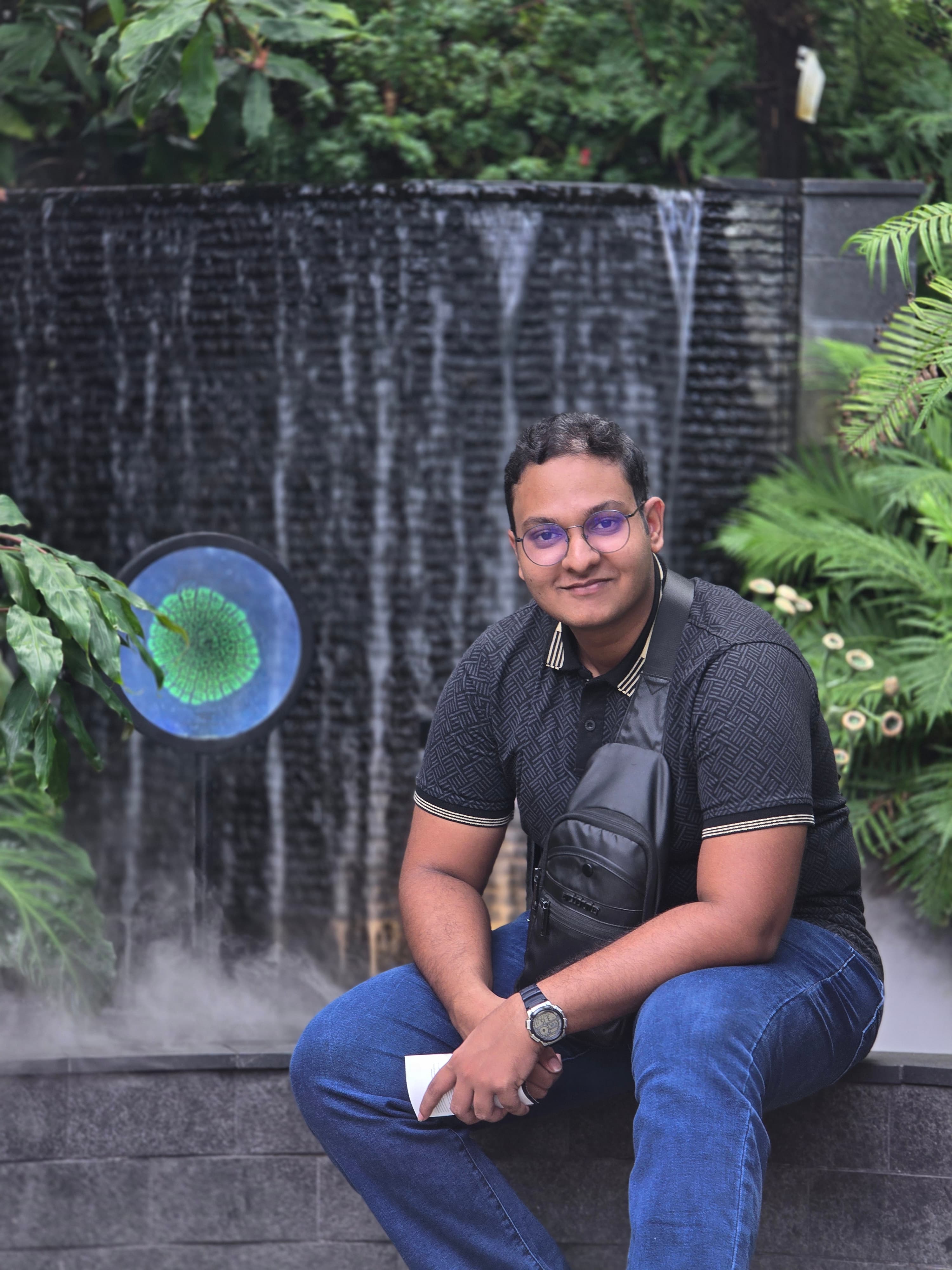 Isira Edirisinghe seated in front of a garden waterfall